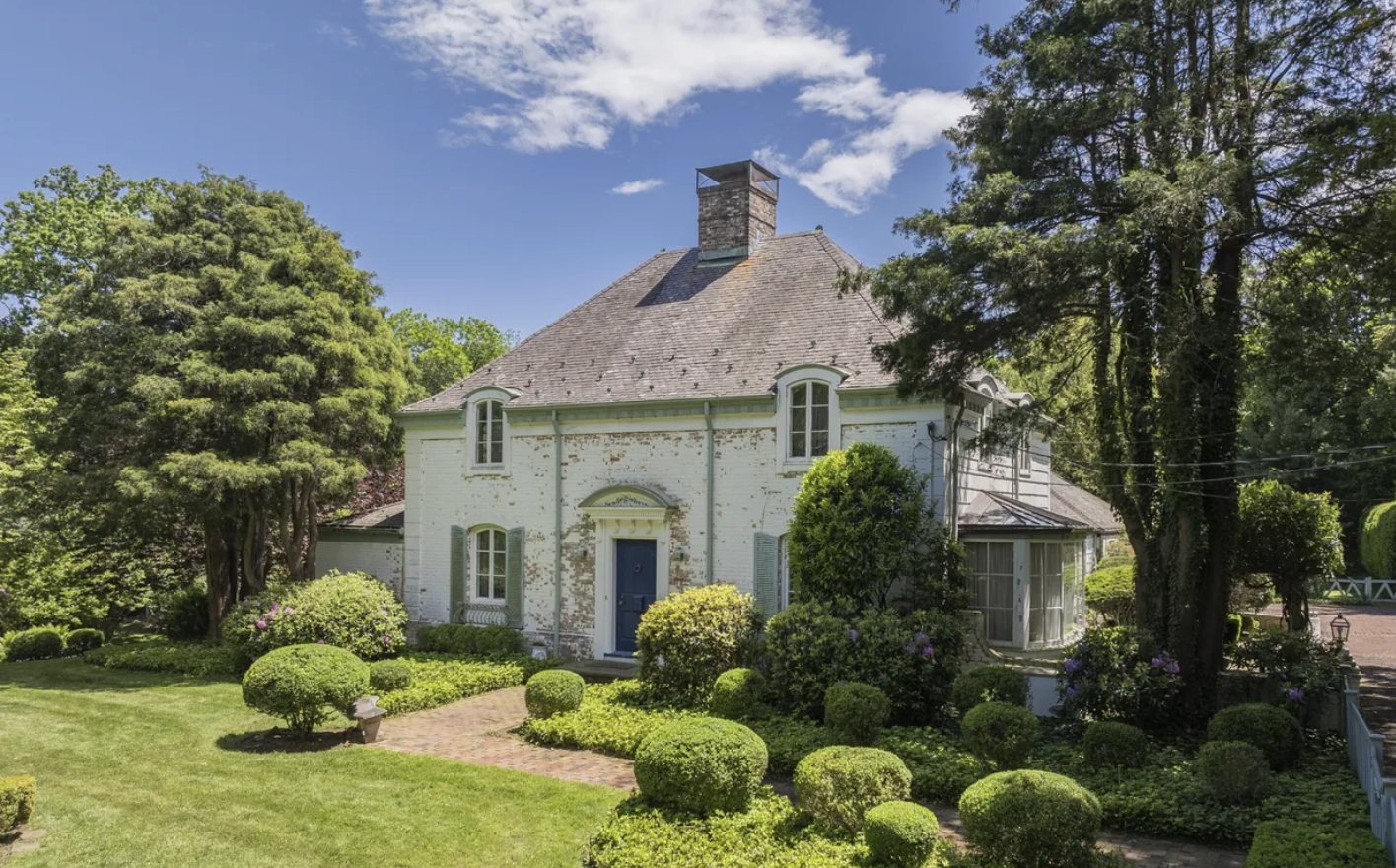White-painted brick Greenwich, Connecticut home built in 1941, with a slate roof, blue front door and manicured boxwood gardens